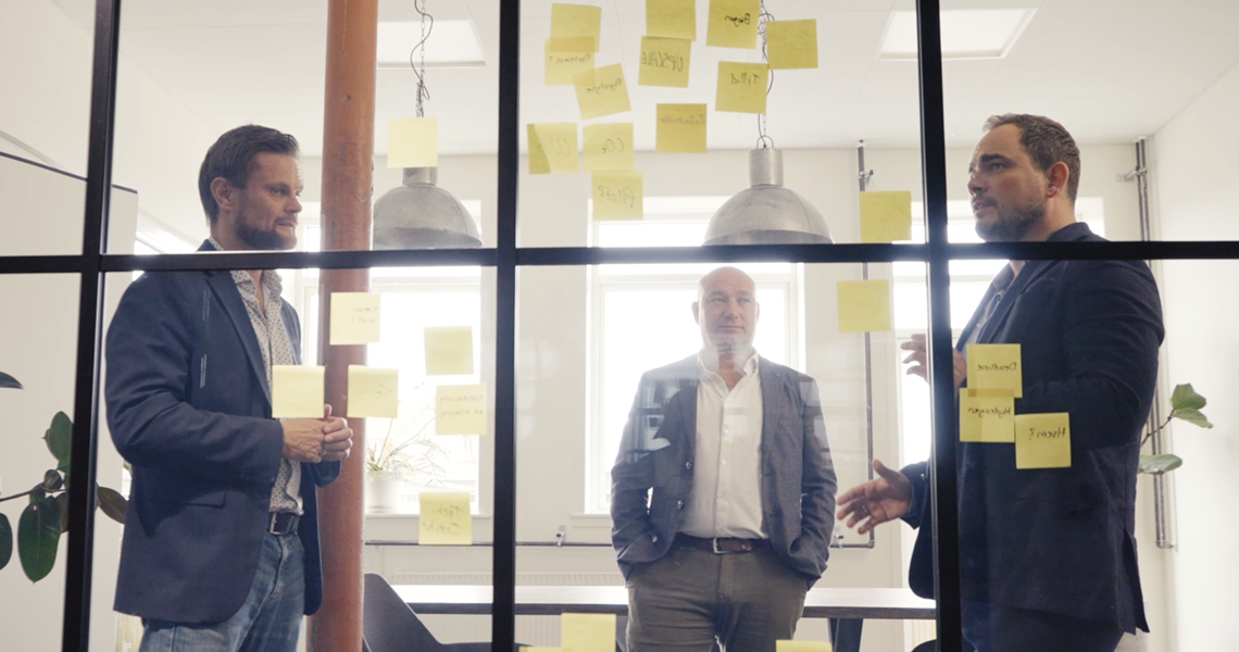 tre mænd foran glasvæg med post its